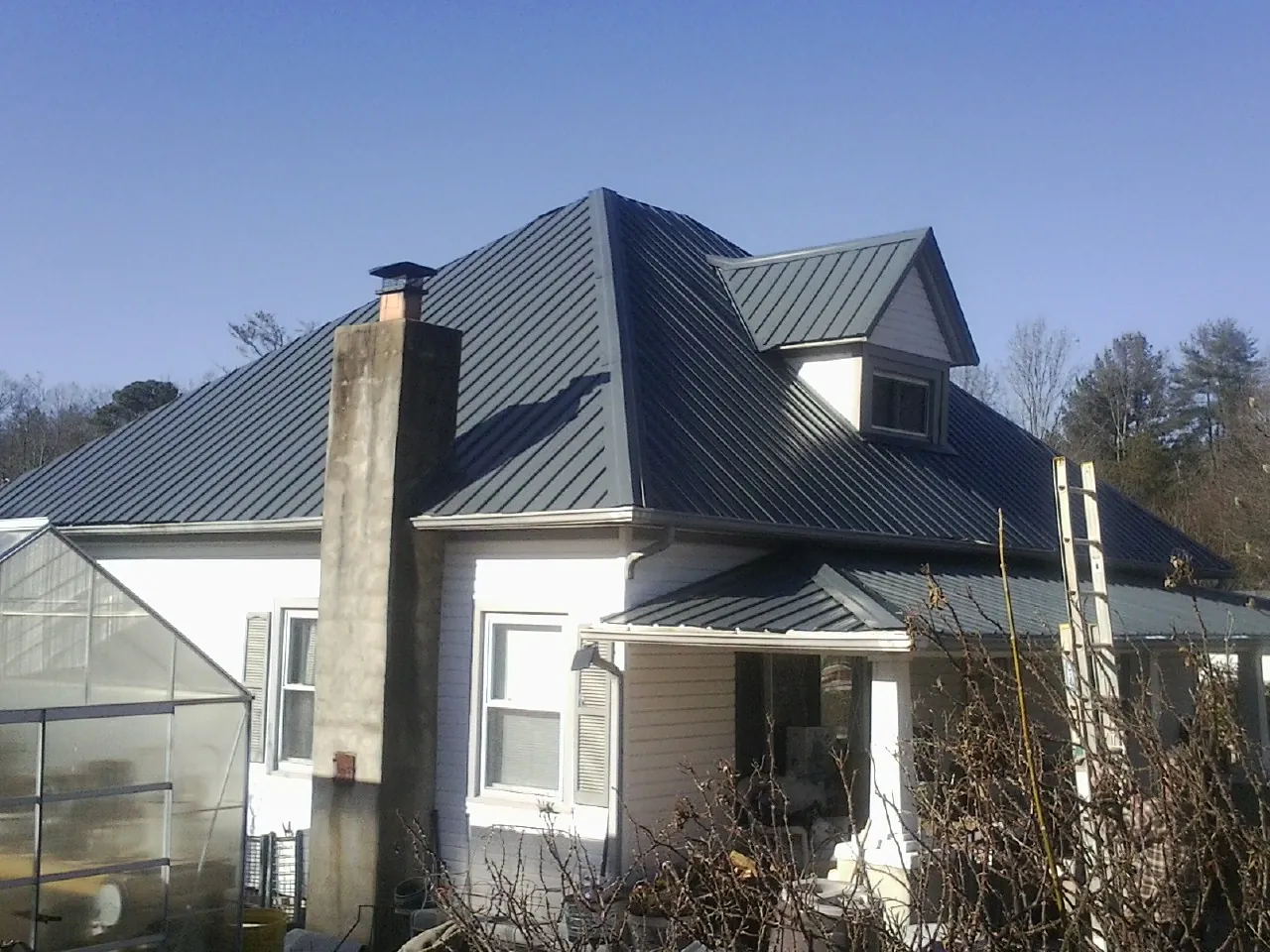 Dark blue standing seam metal roof on a white farmhouse with dormer — Slate & Tile Roof Repair by Roofing Brothers in Mc Donald