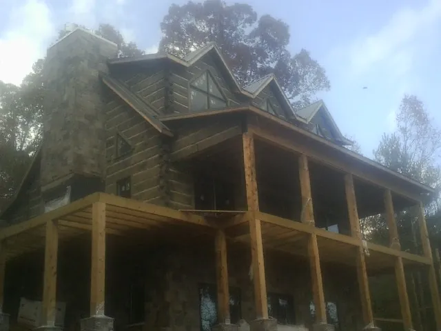 Stone chimney and dormers on a large log home with a timber porch in Mc Donald